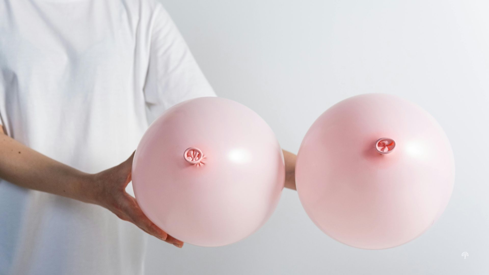 Woman in a white shirt holding two pink balloons symbolizing breast health and raising awareness of the connection between breast cancer treatment and lymphedema.