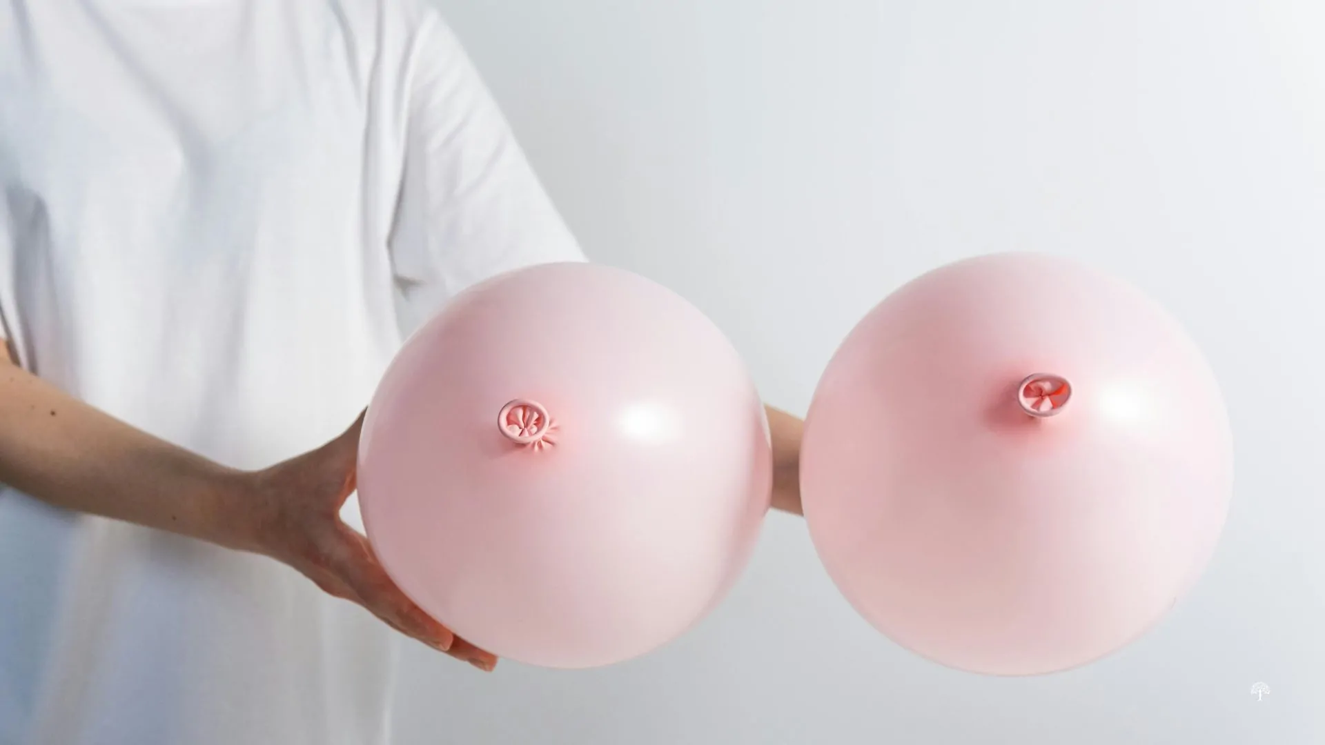 Woman in a white shirt holding two pink balloons symbolizing breast health and raising awareness of the connection between breast cancer treatment and lymphedema.